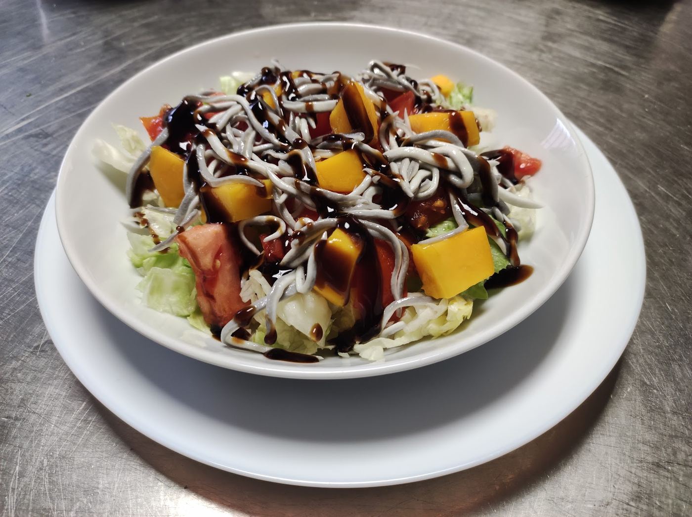 Ensalada templada con gulas y mango, servida en un plato amplio.